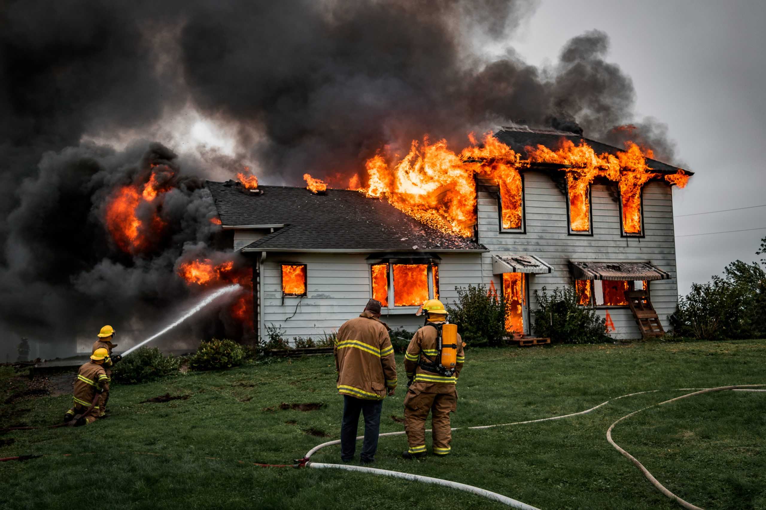Firefighters extinguishing house fire with hoses.